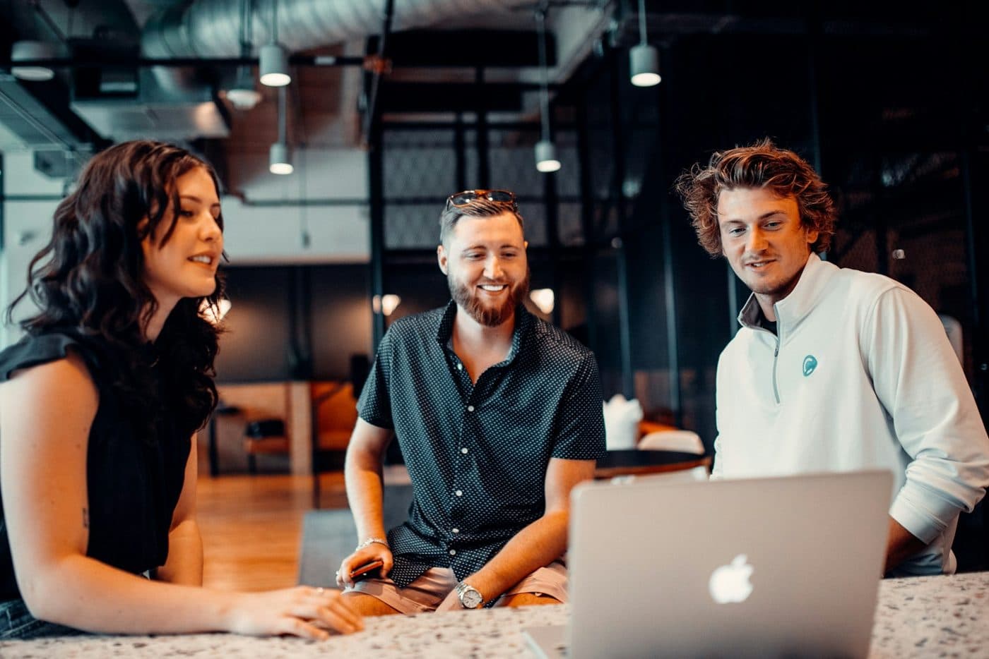 Trois collègues souriant devant un ordinateur portable au bureau